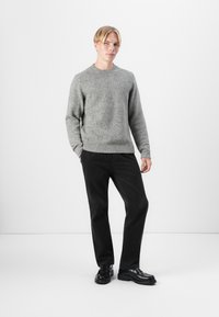 Gray knit sweater with a crew neck and ribbed hem, paired with black corduroy pants. Black shoes with a chunky sole complete the outfit.