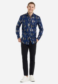 Camisa navy con patrón de árbol dorado, de manga larga y diseño abotonado, combinada con pantalones negros y zapatillas blancas.