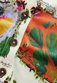 Boutons marron sur tissu blanc avec des motifs floraux et de feuilles colorés en vert, orange, violet et jaune.