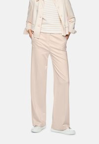 Person wearing beige wide-leg trousers, matching blazer, striped shirt, hands in pockets, and white sneakers against a plain background.