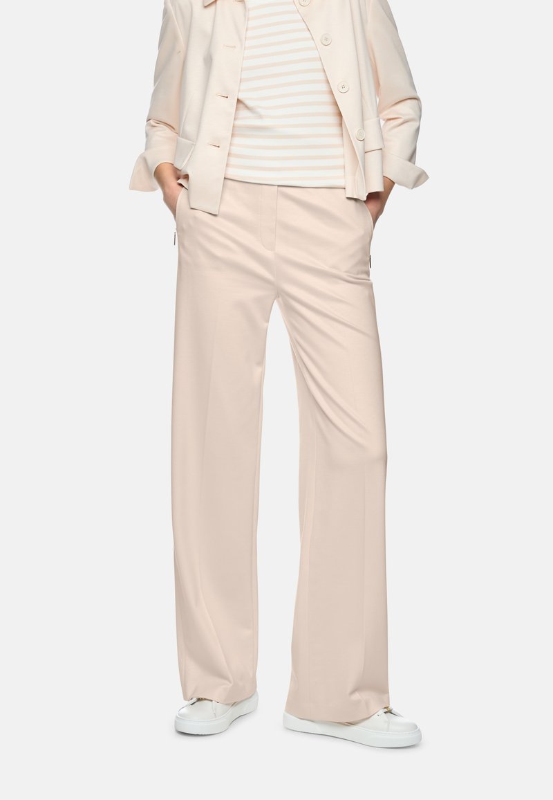 Person wearing beige wide-leg trousers, matching blazer, striped shirt, hands in pockets, and white sneakers against a plain background.