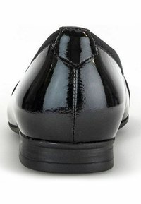 Scarpa in vernice nera con una superficie liscia e lucida, punta tonda e tacco minimo. Design semplice con dettaglio di cucitura centrale.