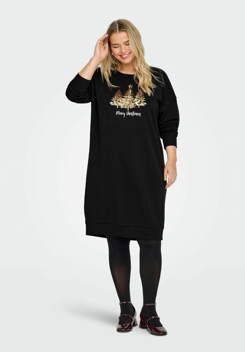 Crna haljina, dukserica s okruglim izrezom, dugim rukavima i zlatnim vezenim dizajnom božićnog drvca. Uparena s crnim tajicama i crvenim cipelama.