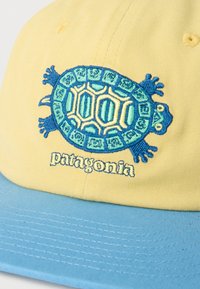 Κίτρινο και μπλε καπέλο με κεντητό σχέδιο χελώνας και λογότυπο "patagonia" στο κέντρο του μπροστινού πάνελ.