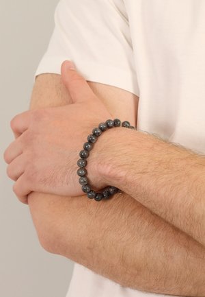 A black stone bead bracelet featuring smooth, round beads with a glossy finish, worn on a wrist, against a neutral background.