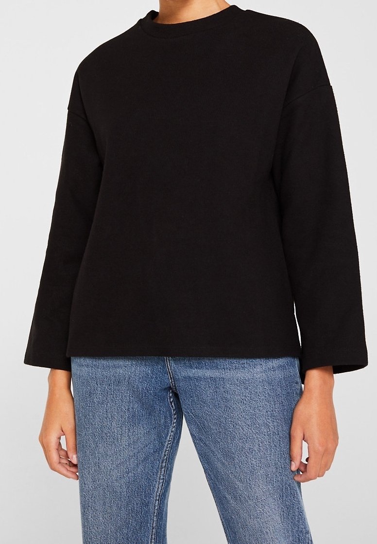 Sweat-shirt noir à manches longues avec un col rond, présentant une coupe décontractée et une texture côtelée, associé à un jean en denim bleu clair.