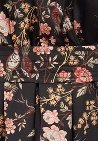 Tela negra con un patrón floral que incluye flores rosas, hojas verdes y pájaros. Diseño plisado con un detalle texturizado en la cintura.
