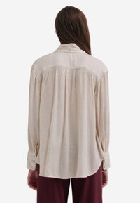 Lichtbeige langemouwhemd met een ontspannen pasvorm, zachte textuur, knoopmanchetten en een geplooide achterkant.