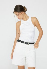 Biała rypsowa tank top z perforowanym wzorem, zestawiony z białymi szortami z wysokim stanem i czarnym paskiem z srebrną klamrą.