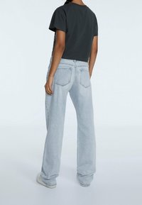 Camiseta negra de corte cropped combinada con jeans de pierna ancha de un azul claro. Los jeans tienen un lavado desgastado y bolsillos traseros, completados con zapatillas blancas.