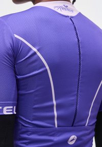 Person trägt ein strukturiertes lila Radtrikot mit weißen Paspeln, schwarzen Ärmeln darunter und "Anima" am hinteren Kragen.