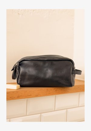 Schwarz Leder Kulturbeutel mit rechteckiger Form, Reißverschluss, seitlichem Griff und geprägt Logo auf der Vorderseite, platziert auf einer Holzoberfläche.