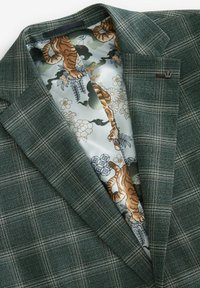 Blazer a quadri verdi con fodera in seta liscia che presenta un motivo di tigre e fiori. Include un sottile accento metallico sul risvolto.