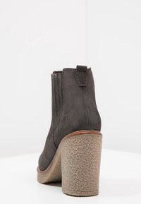 Harmaat mokkasiinit nilkkabuutsit, joissa on teksturoitu vaaleanruskea lohkoepä, sivuvetoketjut ja pieni takanappiyksityiskohta.