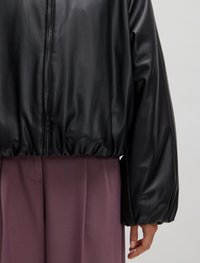 Zwarte faux lederen jas met een hoge hals, geribbelde zoom en volumineuze mouwen, gecombineerd met lichtpaarse broek.