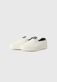 Fehér vászon slip-on cipők, texturált felülettel; sötétkék akcentussal a sarkán és gumi talppal rendelkezik.