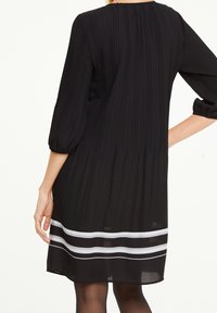 Schwarzes, plissiertes Kleid mit drei Viertelärmeln, verfügt über einen weißen Streifenakzent am Saum und hat eine lockere Passform für Bewegungsfreiheit.