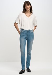 Atpūtas balts V-veida krekls, gaiši zili iegareni džinsi un melni mokasīni. Minimālisma dizains ar gludu tekstūru un bez redzamām izdrukām.