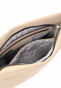 Beige perforierte Ledertasche mit schwarzem Reißverschluss, geöffnet, um das graue Innenfutter aus Stoff mit weißem Aufdruck und einer inneren Reißverschlusstasche zu zeigen.
