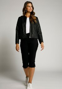 Černá bomber bunda z umělé kůže s prošívaným designem, zapínání na zip, spojená s černými kalhotami capri a bílými teniskami. Jednoduchá, moderní estetika.