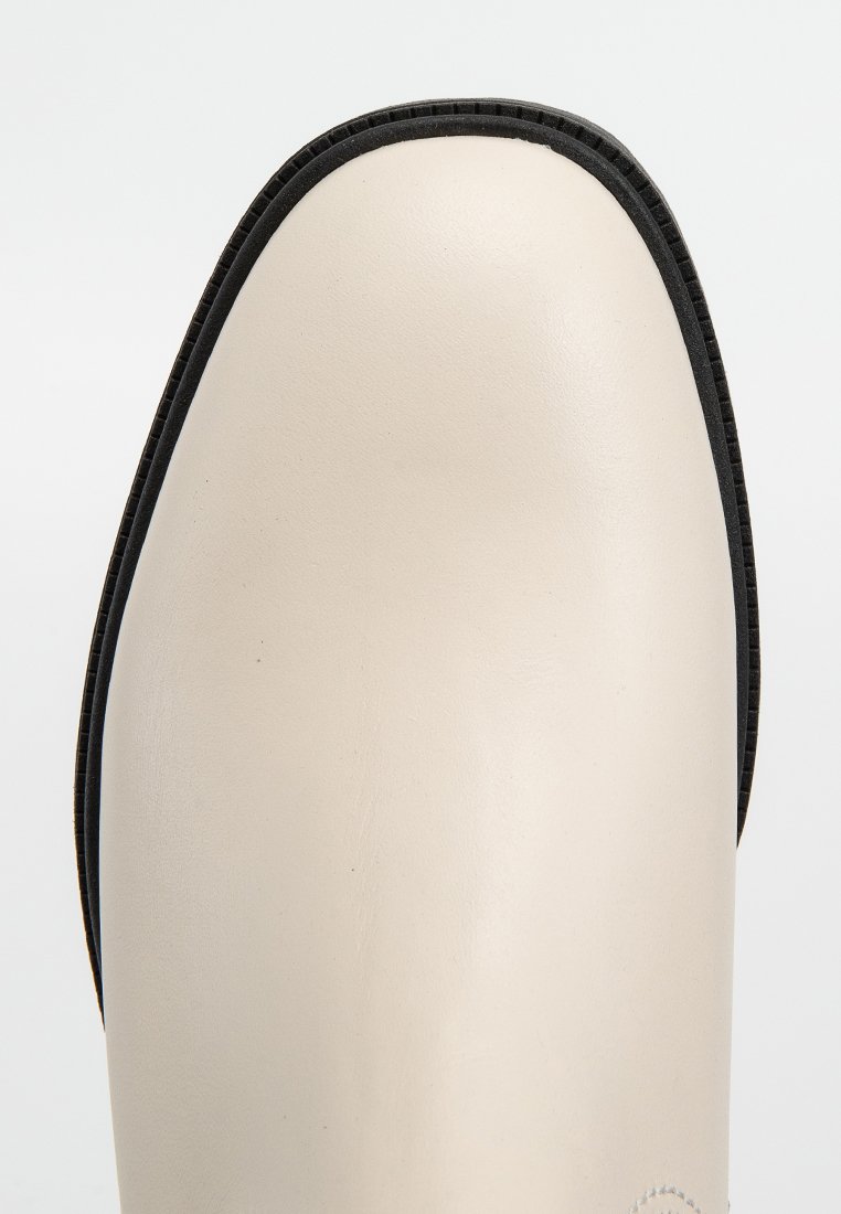 Beige Lederstiefel mit runder Zehenpartie, ausgestattet mit einer schwarzen Gummisohle und -verzierung. Minimalistisches Design mit glatter Textur und ohne Muster.