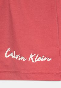 Korallfärgad bomullstyg med mjuk textur, med vit kursiv "Calvin Klein" märkning längs nederkanten.
