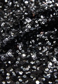 Schwarzer Paillettenstoff mit glänzenden, kreisförmigen Pailletten, die Licht reflektieren und eine strukturierte Oberfläche erzeugen. Der Stoff ist gerafft und geschichtet.