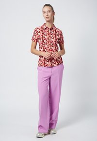 Floral short-sleeve blouse with red and pink flowers on a black background, paired with high-waisted lavender trousers and silver sneakers.
