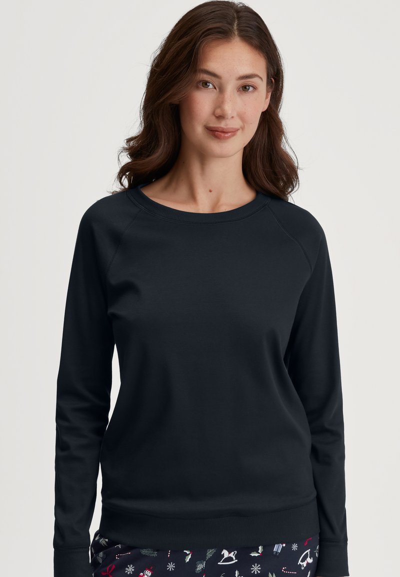 Zwarte sweater met lange mouwen, een ronde halslijn en raglanmouwen. Gladde textuur en ribbelzoom. Draagt met gestreepte pyjamabroek.