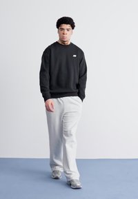 Czarna bluza z małym logo, w zestawieniu z jasnoszarymi spodniami dresowymi i szarymi sneakersami. Gładki materiał i luźny krój.