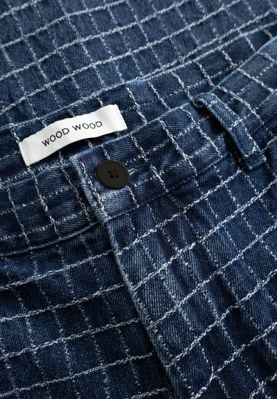 Denim fabric with white grid stitching, black button on waistband, and white label reading "WOOD WOOD."