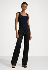 Navy cable knit bodysuit with square neckline paired with black wide-leg trousers and platform sandals featuring a decorative strap.
