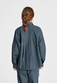 Camisetta grigio scuro con una vestibilità rilassata, schiena plissettata, maniche lunghe e polsini con bottone, realizzata in un tessuto leggero.