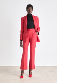 Rød skræddersyet jakkesæt med en struktureret blazer og lige bukser, parret med en sort turtleneck og glinsende røde højhælede sko.