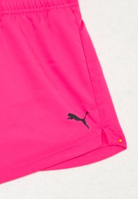 Roza športna kratka hlače iz lahkotnega materiala, z bočnimi razporki in črnim logotipom Puma na spodnjem levem delu.