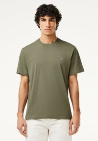 T-shirt in cotone verde oliva con scollatura rotonda. Presenta maniche corte e un piccolo logo verde e bianco sul lato sinistro del petto.
