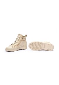 Beige ankle boots in textured leather, featuring a zip closure, flat rubber sole with a patterned tread, and metal eyelets for laces.