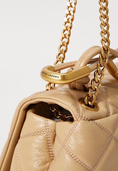 Vadderad handväska i beige läder med ett guld-chain handtag och uttalad hårdvara. Anmärkningsvärd sömnad och logodetalj på låset.