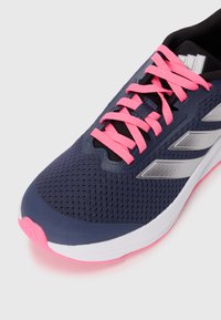 Baskets de sport bleu marine avec des lacets roses, une tige en maille texturée, des accents en argent et une semelle intermédiaire blanche avec une semelle extérieure rose.