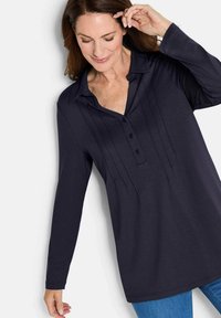 Camicia a maniche lunghe blu navy con colletto, patta con bottoni e pieghe verticali. Tessuto morbido, vestibilità comoda e orlo leggermente curvo per il comfort.