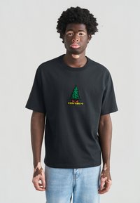 Μαύρο βαμβακερό t-shirt με πράσινο κεντημένο λογότυπο δέντρου και την επιγραφή "CONVERSE" σε κίτρινο από κάτω. Κανονική εφαρμογή με κοντά μανίκια. Ανοιχτό μπλε παντελόνι τζιν.