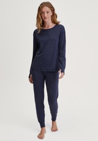 Marine blauwe tweedelige pyjama set gemaakt van zachte stof; langesleeve top met ronde hals en taps toelopende broek met elastische manchetten, met een relaxte pasvorm.