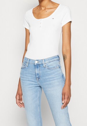 Biały body z krótkim rękawem, dekoltem w serek i trzema zatrzaskami, zestawiony z jasnoniebieskimi dżinsami.