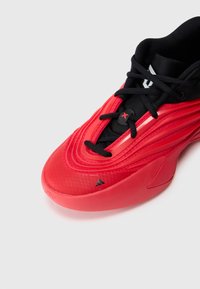 Chaussure de sport rouge et noire avec des lacets, des détails de design en relief et un petit logo Adidas noir près de l'orteil sur un fond blanc.