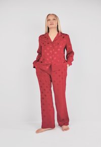 Ensemble de vêtements d'intérieur rouge à pois en tissu lisse ; comprend une chemise boutonnée et un pantalon ample à coupe décontractée.