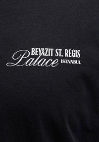 Μαύρο ύφασμα με λευκό κείμενο που γράφει «Beyazit St. Regis Palace Istanbul» σε ανάμεικτες γραμματοσειρές με serif και καλλιγραφικά.