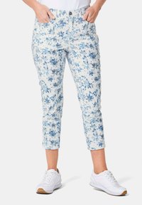 Witte capripantalon met bloemenprint in blauwe kleuren, voorzien van zijzakken en een getailleerd ontwerp. Geselecteerd met witte sportchoenen.