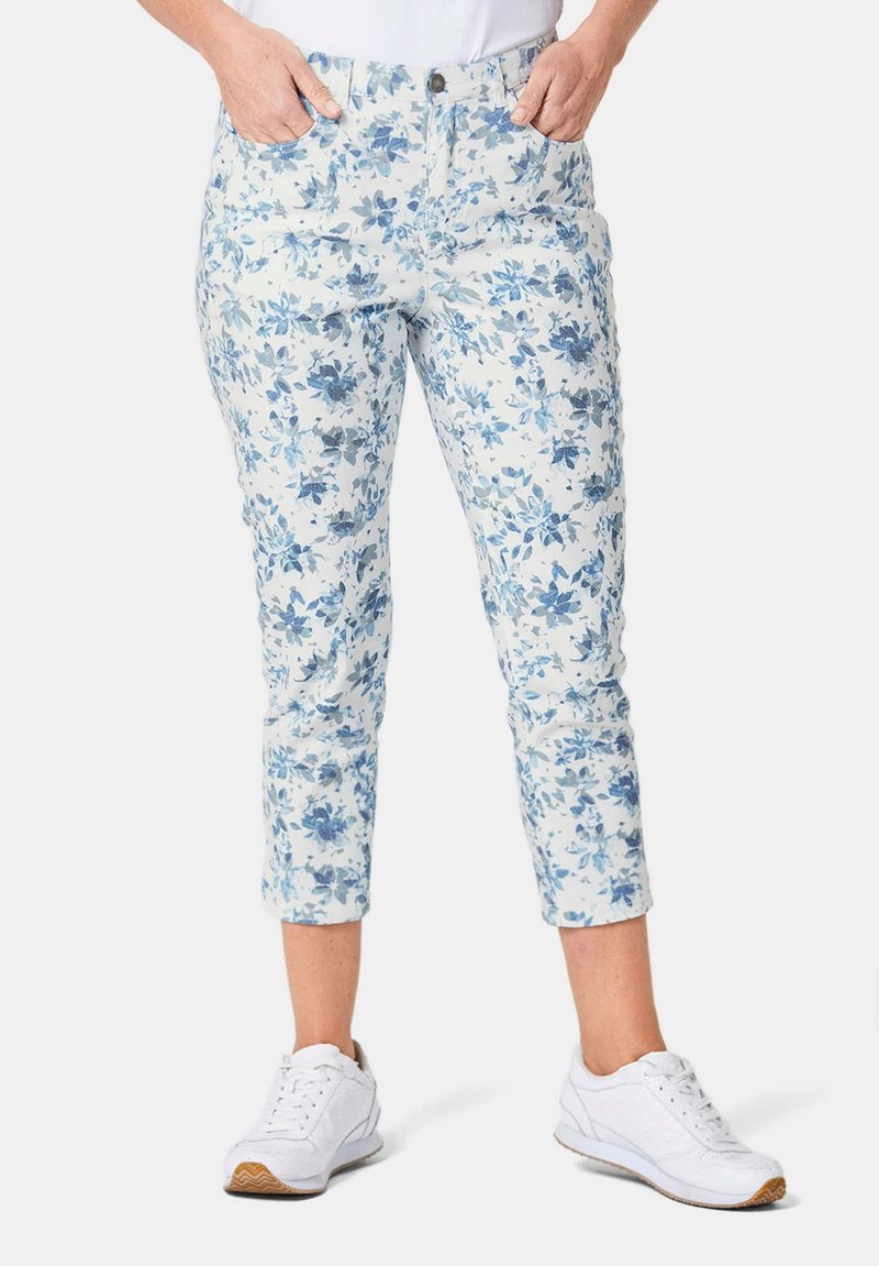 Witte capripantalon met bloemenprint in blauwe kleuren, voorzien van zijzakken en een getailleerd ontwerp. Geselecteerd met witte sportchoenen.