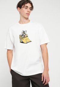 T-shirt bianco in cotone con una grafica colorata di un personaggio su una rampe da skate. Vestibilità ampia, maniche corte e scollo tondo.