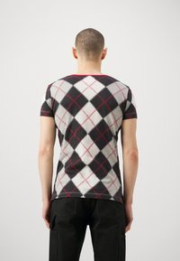 Short-sleeve T-shirt with a black, grey, and white argyle pattern, featuring red diamond outlines. Material appears soft and fitted.